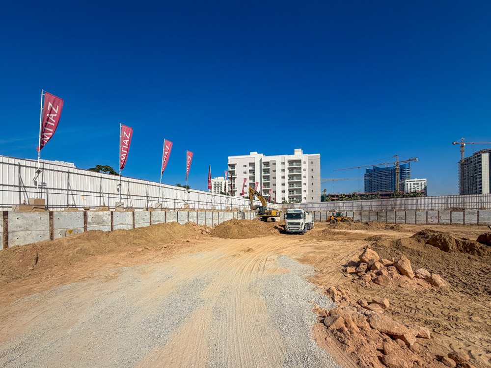 Cove Grand By Imtiaz Construction site with earth moving equipment, gravel pathways, and buildings in the background under a blue sky.